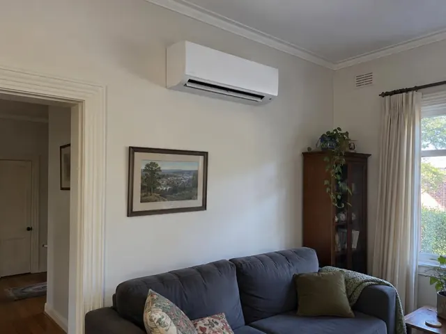 Wall-mounted split system above a couch in a living room with framed art and a window in Blair Athol